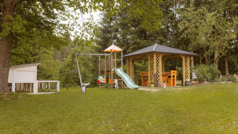 A playground with swings, slide and pavilion in a green garden.