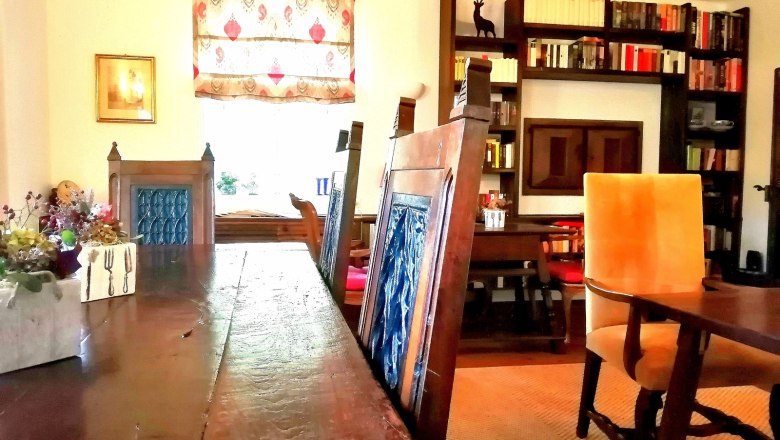 A cozy breakfast room with wooden table, blue chairs, bookshelf and decorative window.