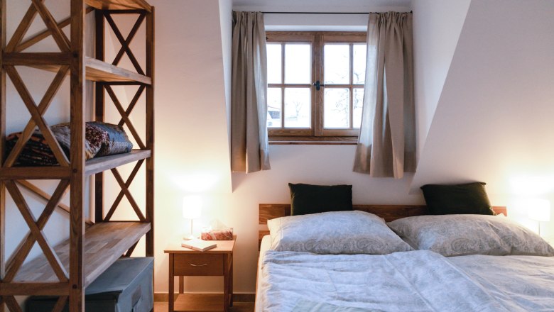 Cozy bedroom with double bed, wooden shelf and bedside lamp.