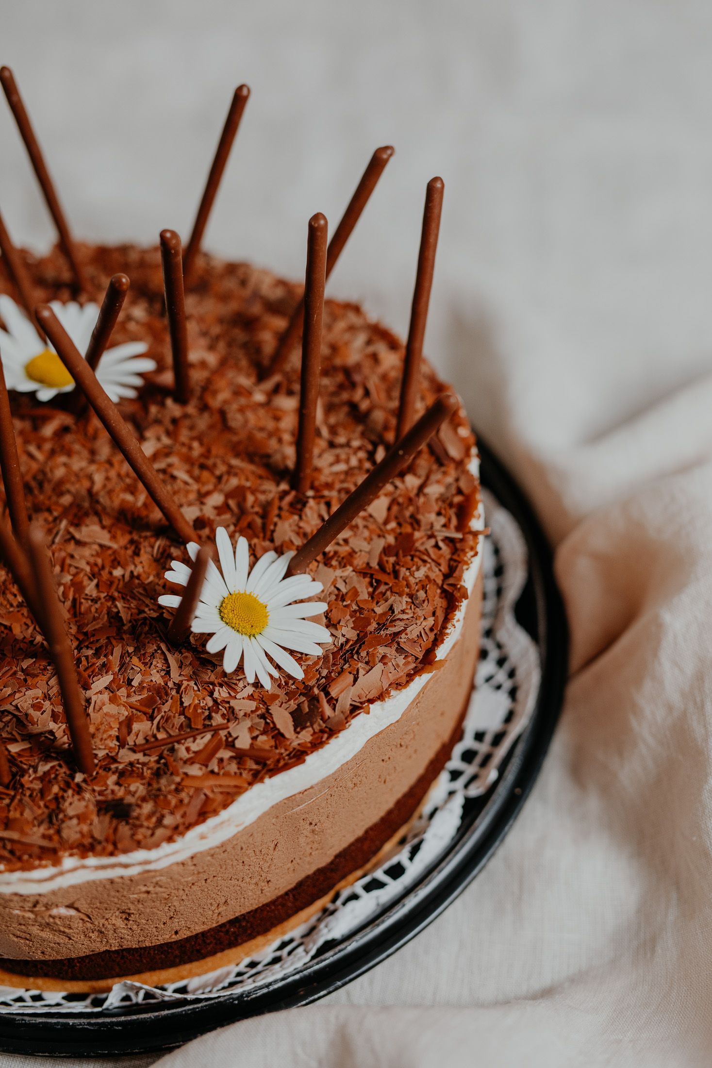 Chocolate cake decorated with chocolate sticks and daisies.