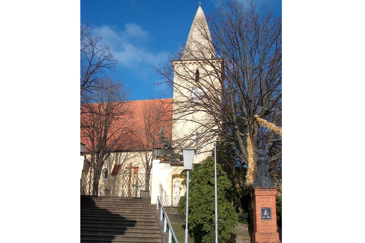Parish church with tower and red roof tiles, surrounded by trees and steps in the foreground.
