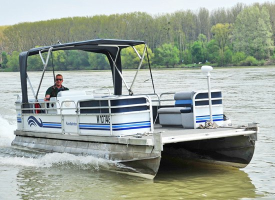 A small motorboat sails on a river, surrounded by trees on the bank.