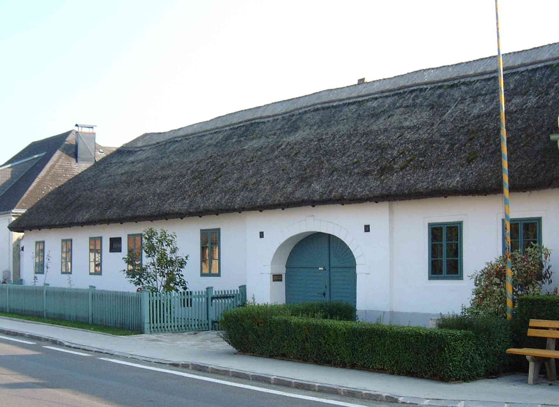 The house where Joseph Haydn was born in Rohrau, Austria, with a thatched roof and blue windows.
