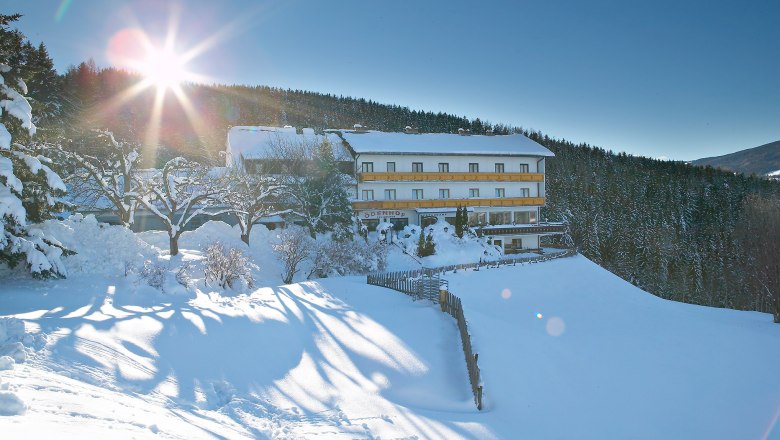 A snow-covered building with the inscription 'Ödenhof' in a wintry landscape, surrounded by trees and bright sunshine.