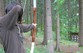 Person shoots at a target with a bow in the forest.