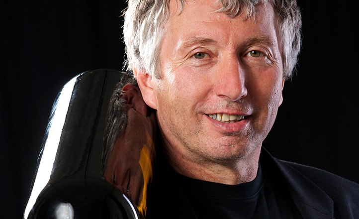 Man with gray hair holding a large wine bottle on his shoulder.
