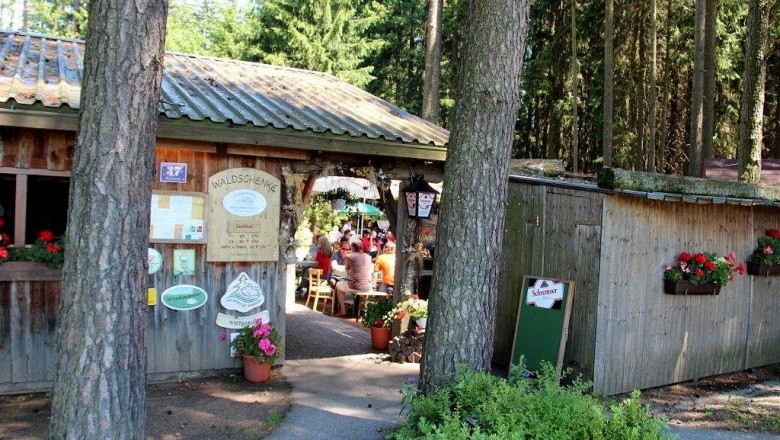 Entrance to a forest tavern with wooden hut and flowers.