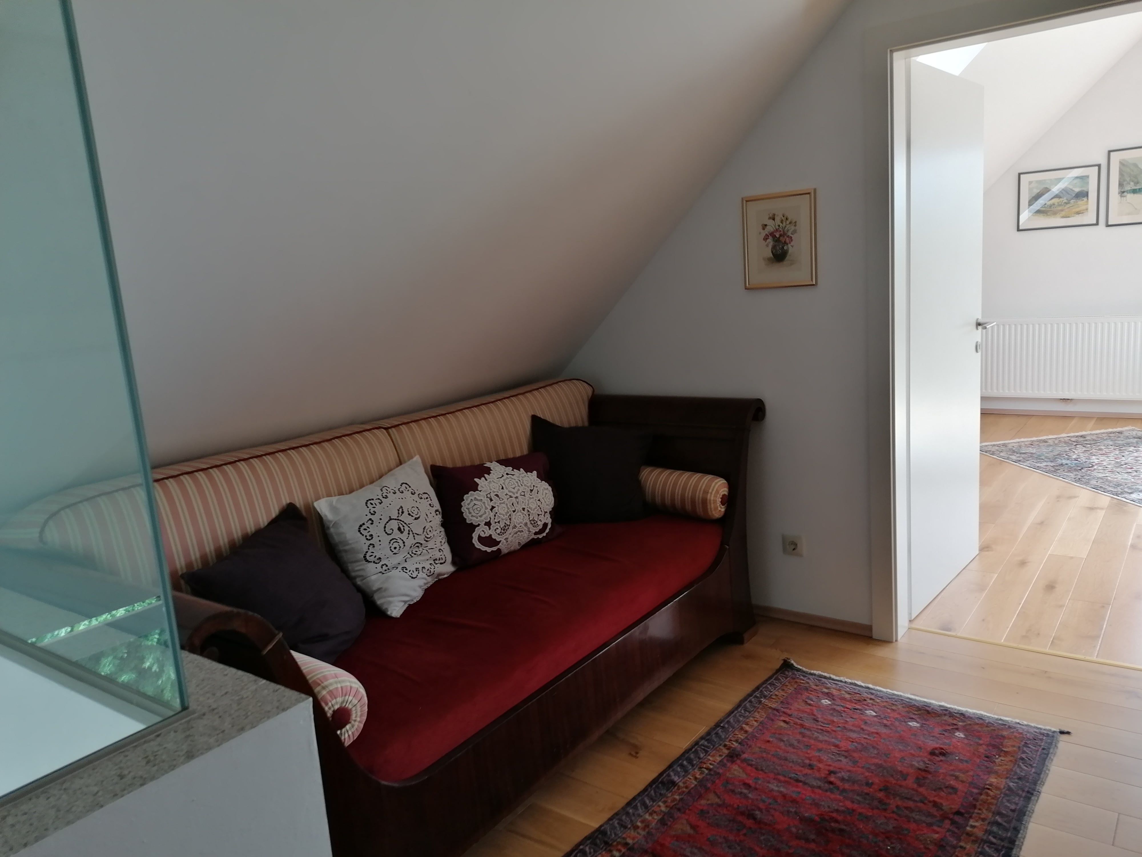 A sofa with cushions stands in a hallway in front of an open door to a bright room.