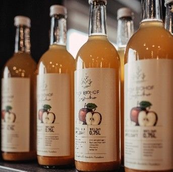 Several bottles of cloudy apple juice or apple cider are lined up next to each other; in the foreground is a bottle with a label indicating 0.75 liters.