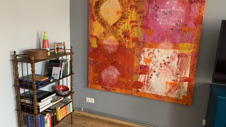 A small bookshelf with books and decorations next to a large, colorful painting on the wall.