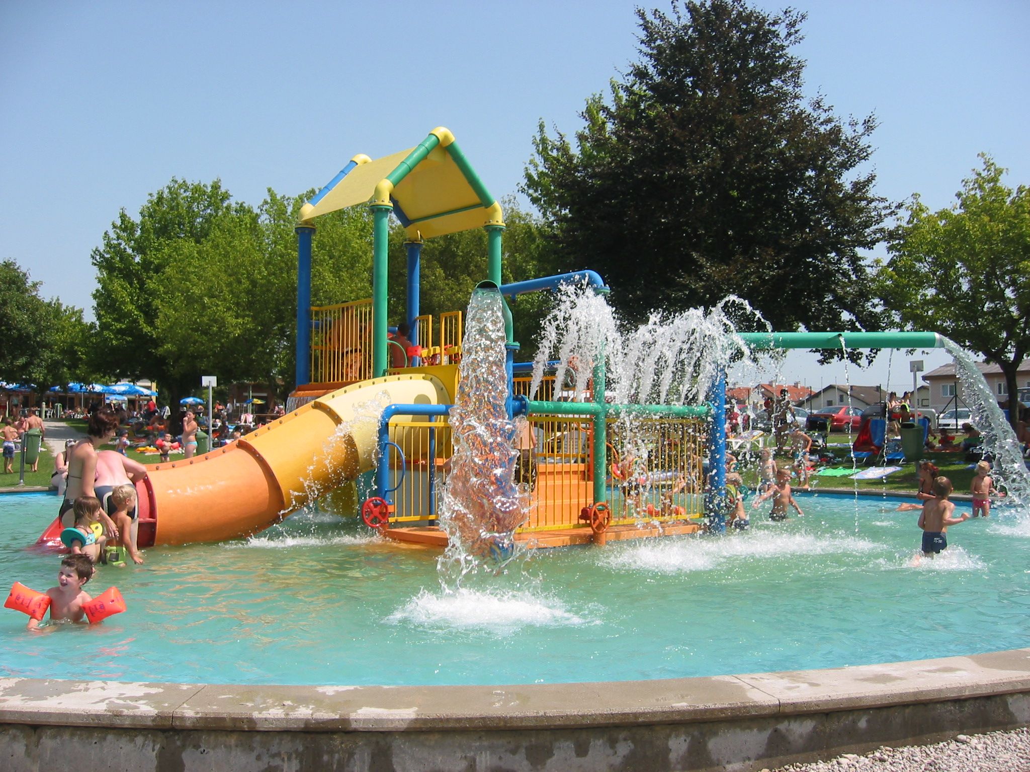 Children play in a water play garden with slides and water fountains.