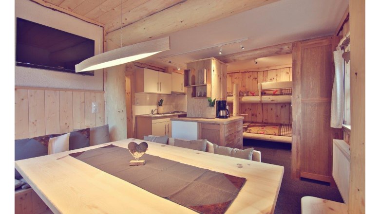 Interior view of a cozy chalet with wooden furniture, dining table, kitchen and bunk beds.