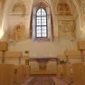 Interior view of a castle chapel with frescoes and wooden benches.