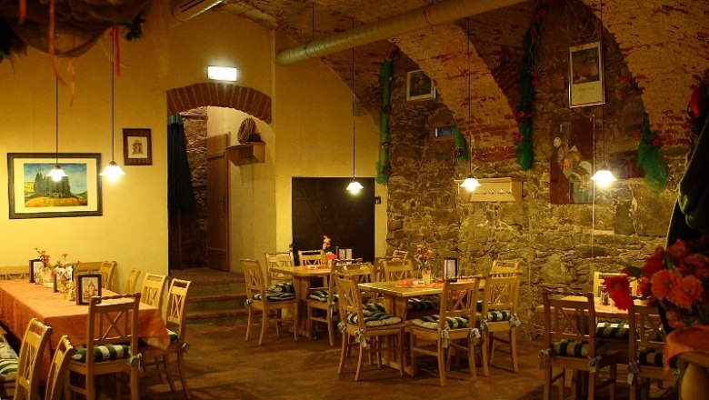 Cozy dining room with wooden tables and chairs, decorated with flowers and pictures on the walls.