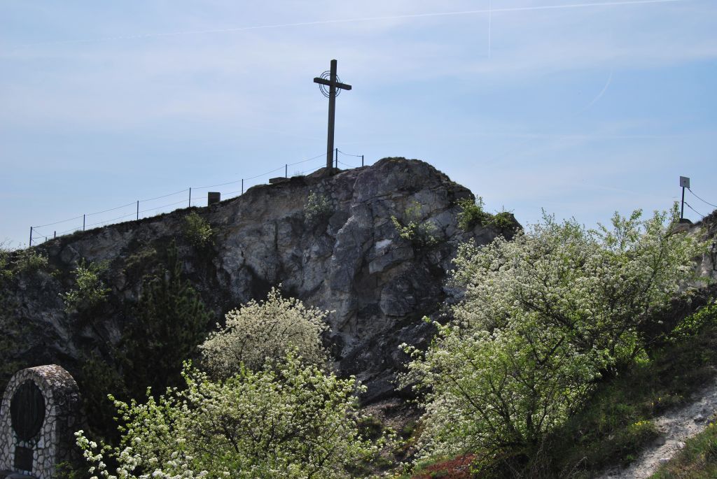 A cross stands on a hill with blossoming trees in the foreground.