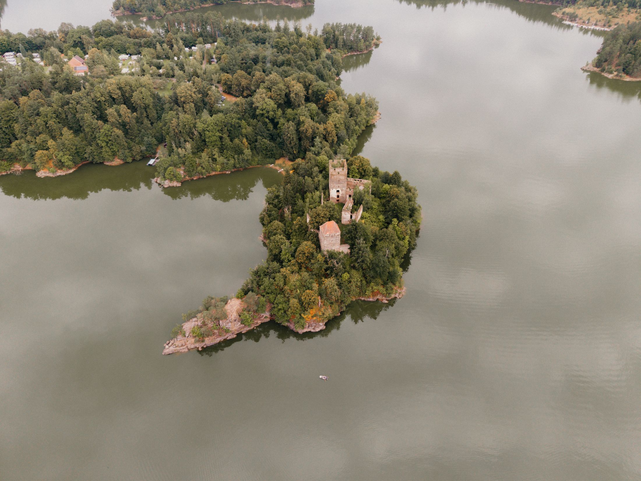 Aerial view of a castle ruin on a wooded island in a lake.