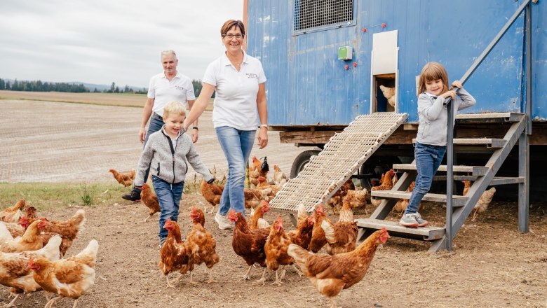 Family with chickens in front of a blue chicken coop in a field.