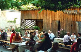 People sit at wooden tables in a cozy courtyard with vines.