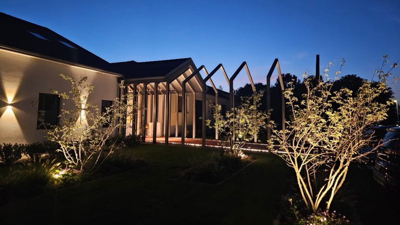 Illuminated building at night with modern structures and trees in the foreground.