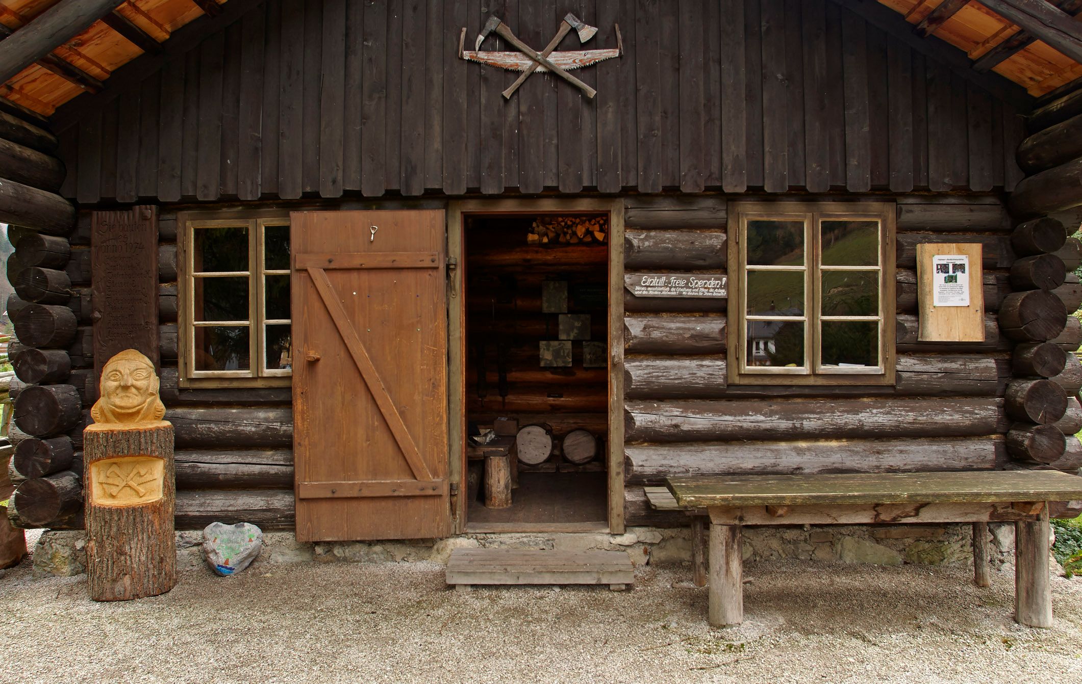 A rustic wooden hut with an open door, wood carving and a table in front of it.