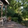 Terrace with table and chairs in front of a vacation home, surrounded by trees and plants.