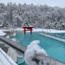 A snow-covered outdoor pool at a thermal spa with red Asian elements and snow-covered trees in the background.