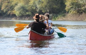 Three people paddling in a red canoe on a river.