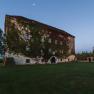 Old building overgrown with ivy, surrounded by meadow and trees, with moon in the sky at dusk.