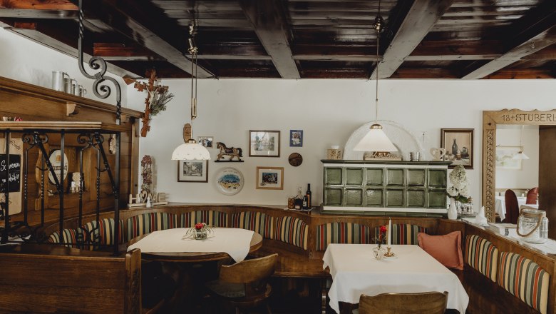 Cozy dining room with wooden furniture, tiled stove and decorative pictures on the wall.