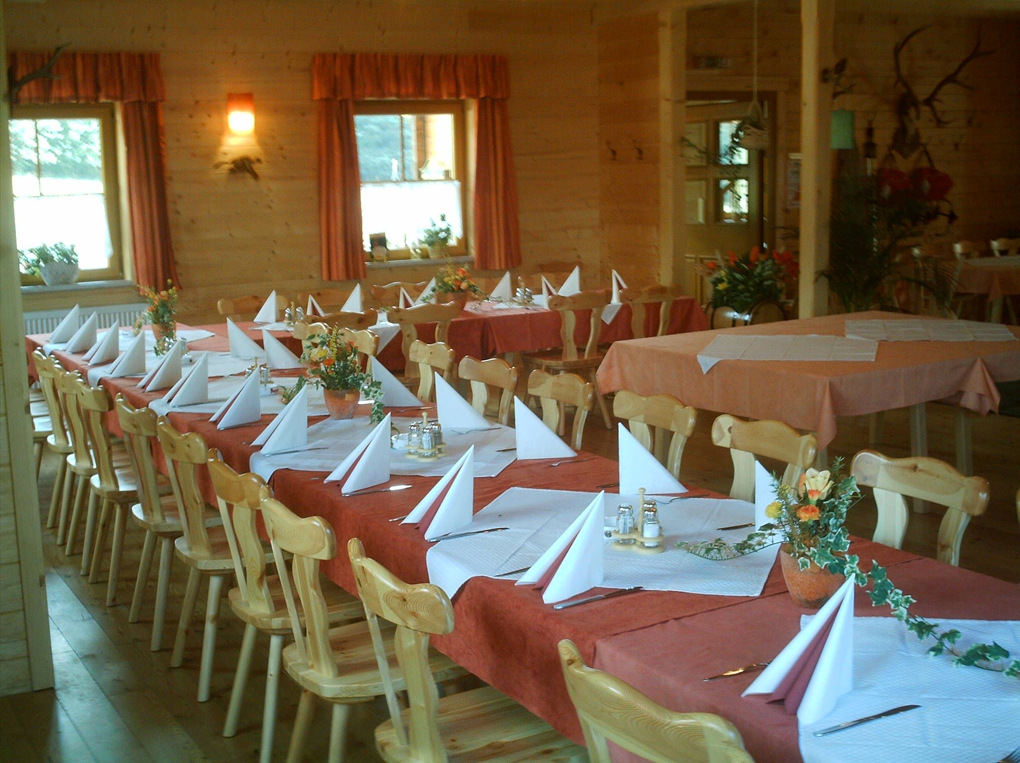 A rustic dining room with wooden furniture, laid tables and decorative flower arrangements.
