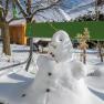 A little snowman sits on a green bench in the snow-covered garden.