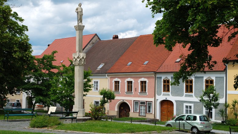 Statue on a pillar in front of colorful houses in Drosendorf-Zissersdorf.