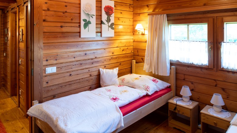 Cozy bedroom with wooden walls, single bed, two bedside tables and windows with curtains.