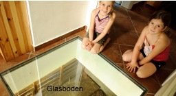 Two children sit next to a glass floor that provides a view of the structures below.