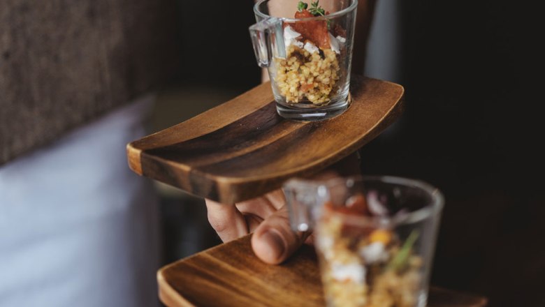 Two small glasses with food on wooden trays, held by one hand.
