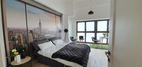 Modern bedroom with large bed, cityscape mural and seating area in front of large windows.