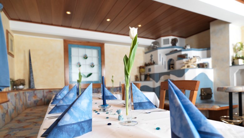 An elegantly laid table with blue napkins and a white tulip in a glass in a cozy room.