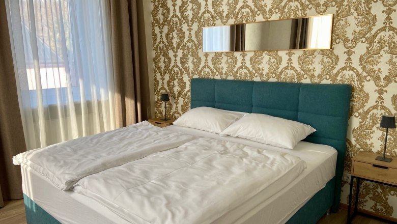 A stylishly furnished bedroom with a large bed, blue headboard and golden wallpaper.