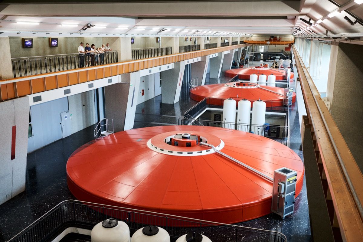 A group of visitors with a tour guide on the visitor walkway above the machine hall of the Ybbs-Persenbeug Danube Power Plant, looking out at the three main turbine units.