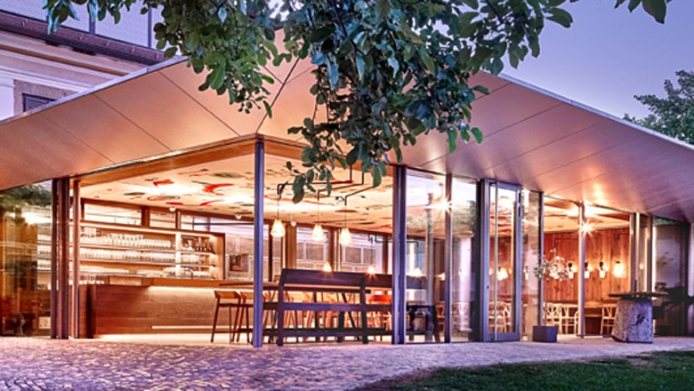 Modern glass façade of a restaurant with illuminated interior and bar.