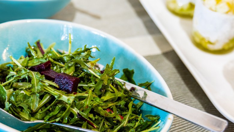 A plate with rocket salad and pieces of beet, next to glasses of dessert.