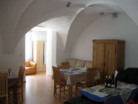 A living room with vaulted ceiling, dining table, chairs and a cupboard.