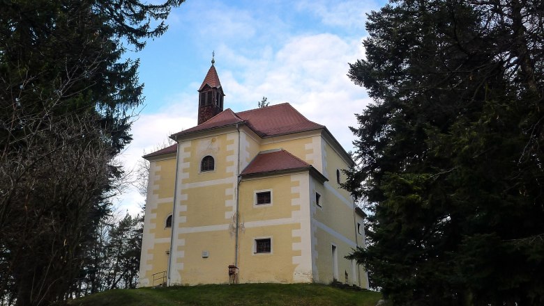 Chapel with yellow façade on a hill surrounded by trees.