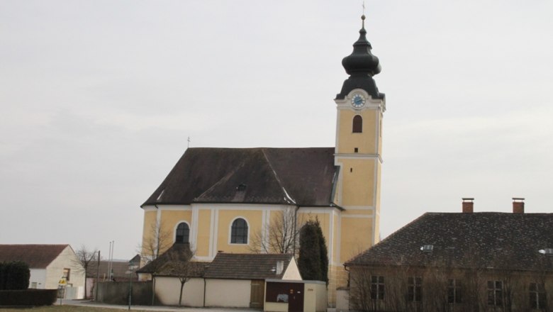 Yellow church with tower and clock in Langenrohr, surrounded by buildings and trees.