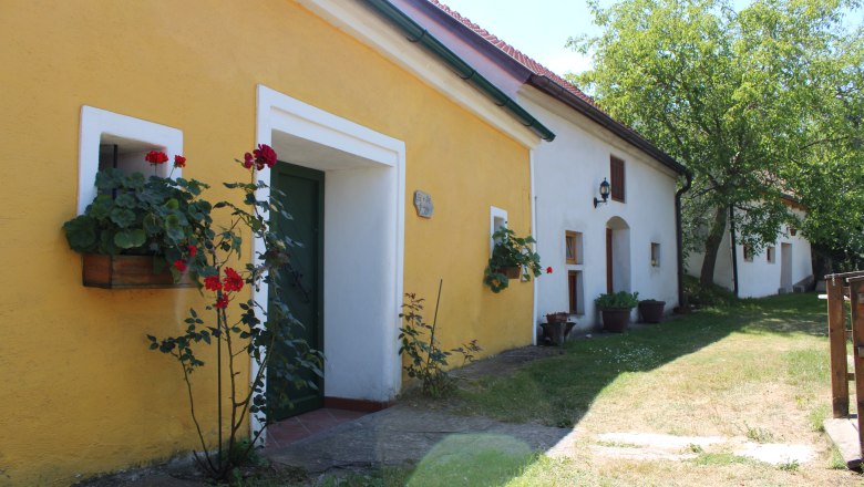 Yellow and white building in a wine cellar lane with flowers and trees.