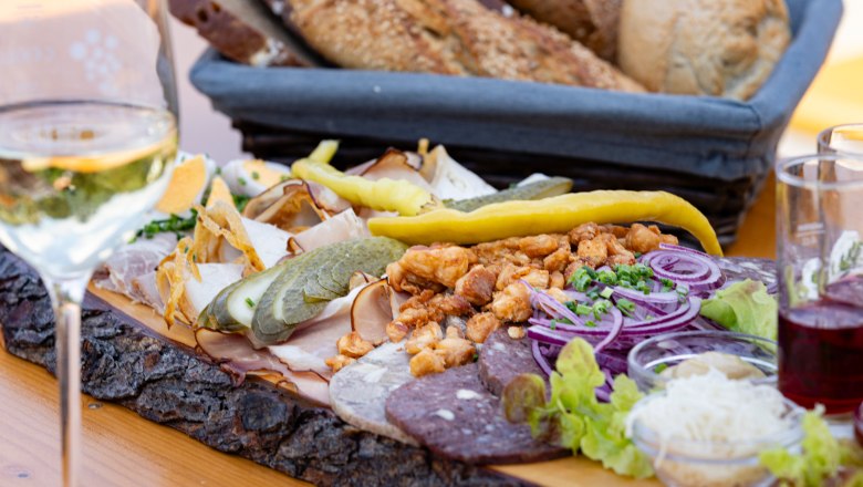 Heurigen platter with cold cuts, onions, gherkins and bread on a wooden table.