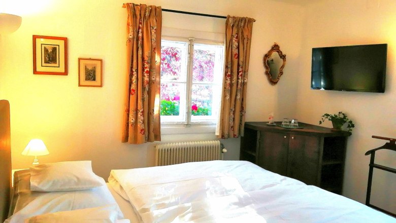 Comfortable double room with bed, TV, window with curtains, pictures on the wall and a small wardrobe.