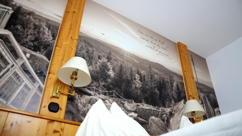 A bedroom with wooden walls and a large mural of a forest and mountains. Two wall lamps are attached to the wooden walls.