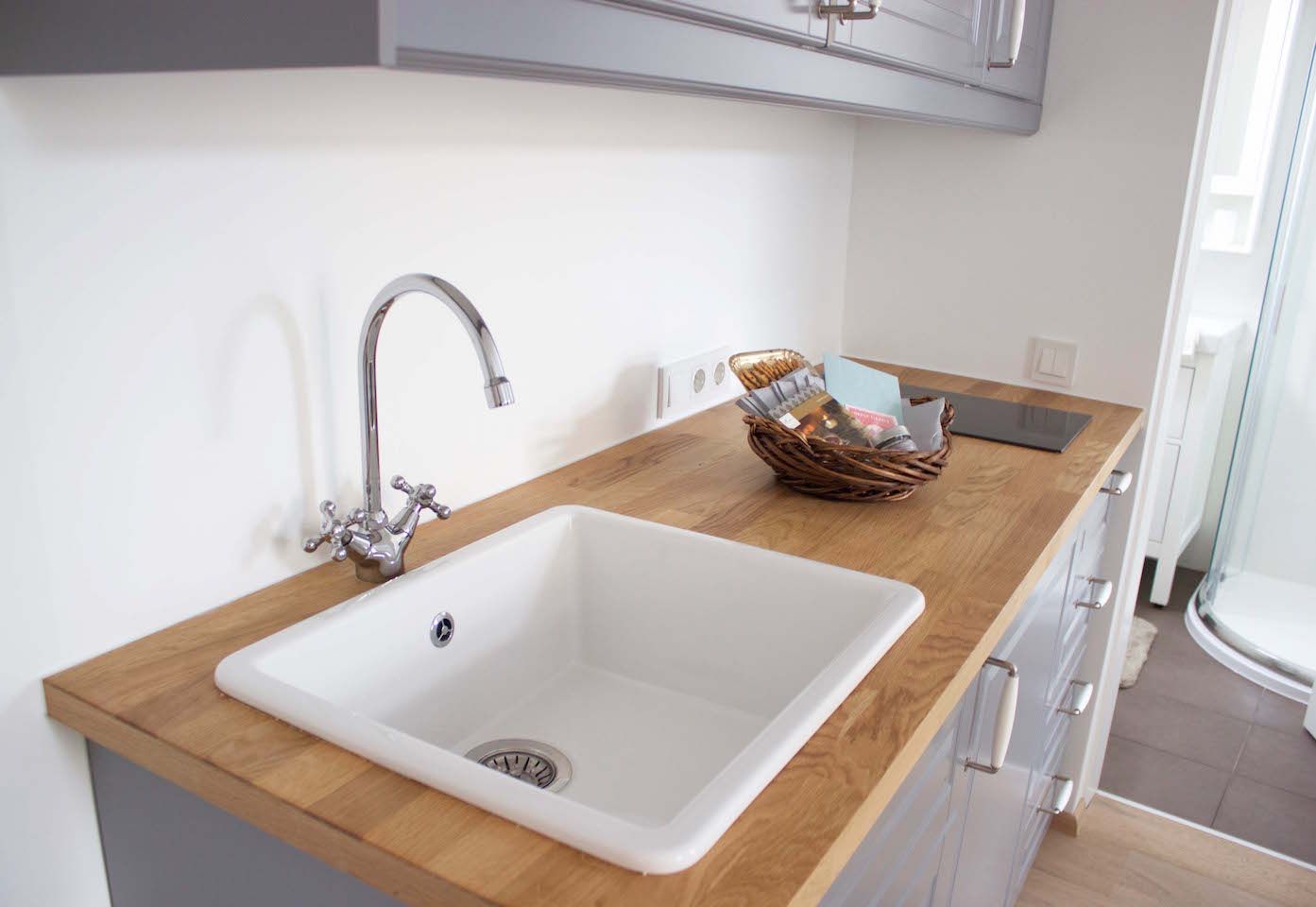 Modern kitchen unit with sink, wooden worktop and basket with utensils.