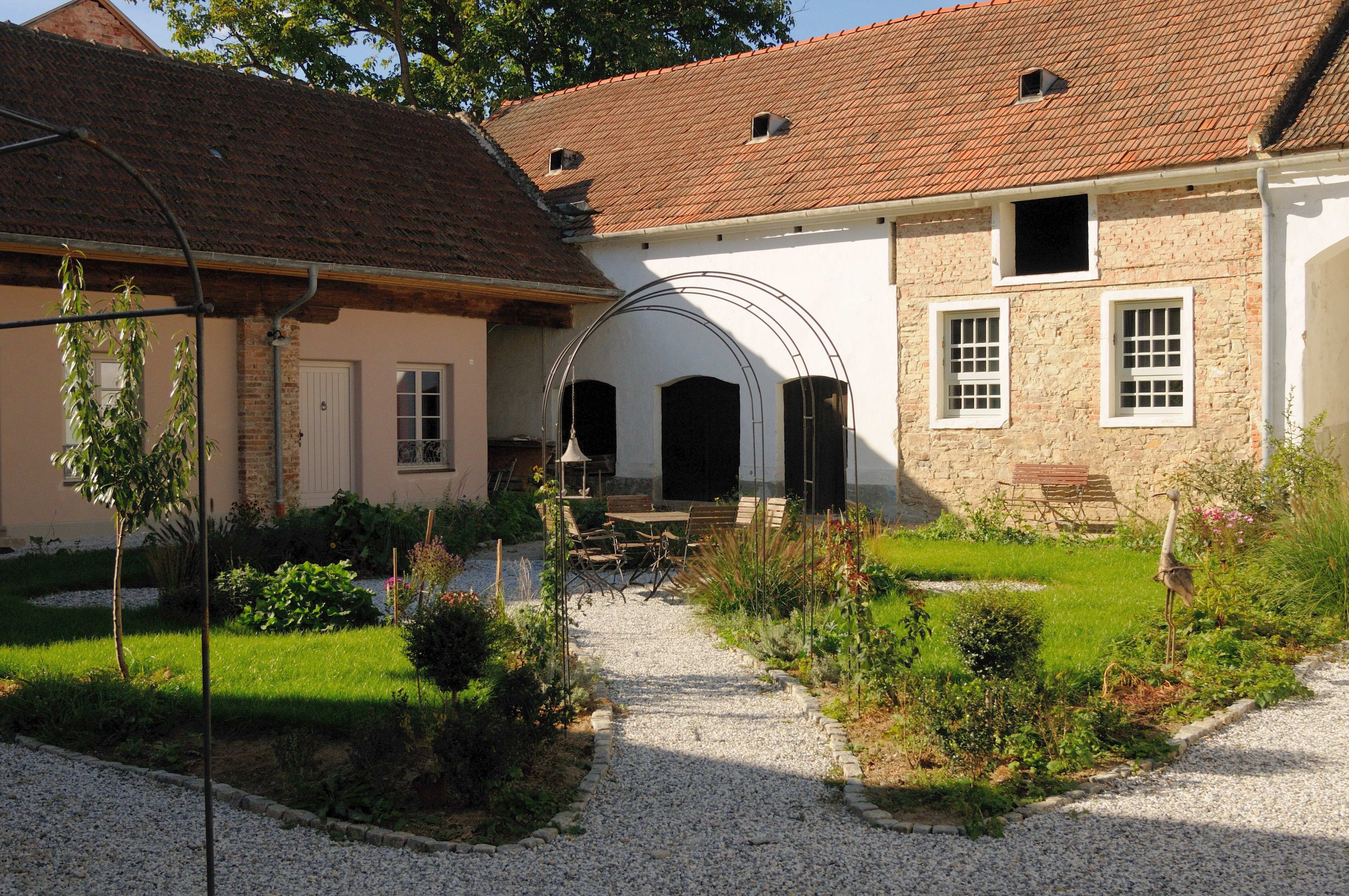 An idyllic inner courtyard with gravel paths, green plants and a seating area under a metal arch.